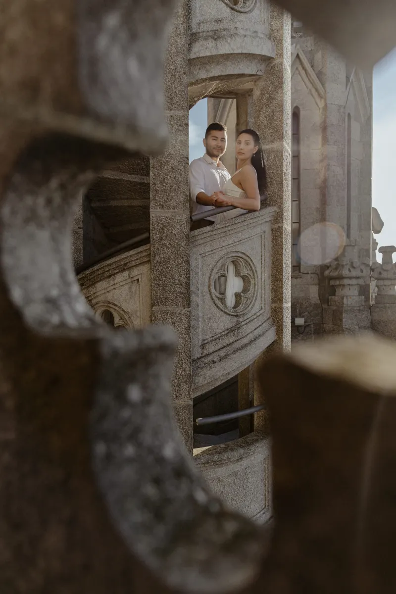 Couple holds hands on a stone spiral staircase, sharing a quiet, romantic moment during their engagement photoshoot.