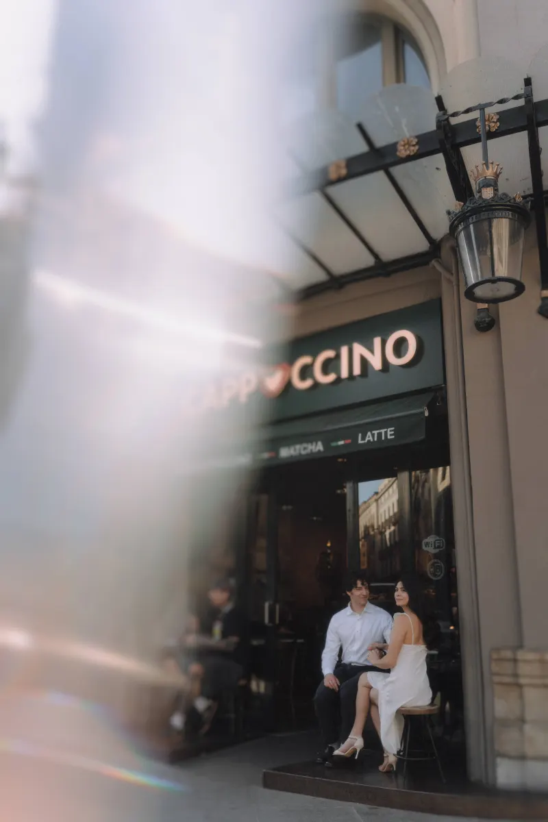 Couple in elegant attire sharing a quiet, romantic moment outside a café during their couples & engagements photoshoot.