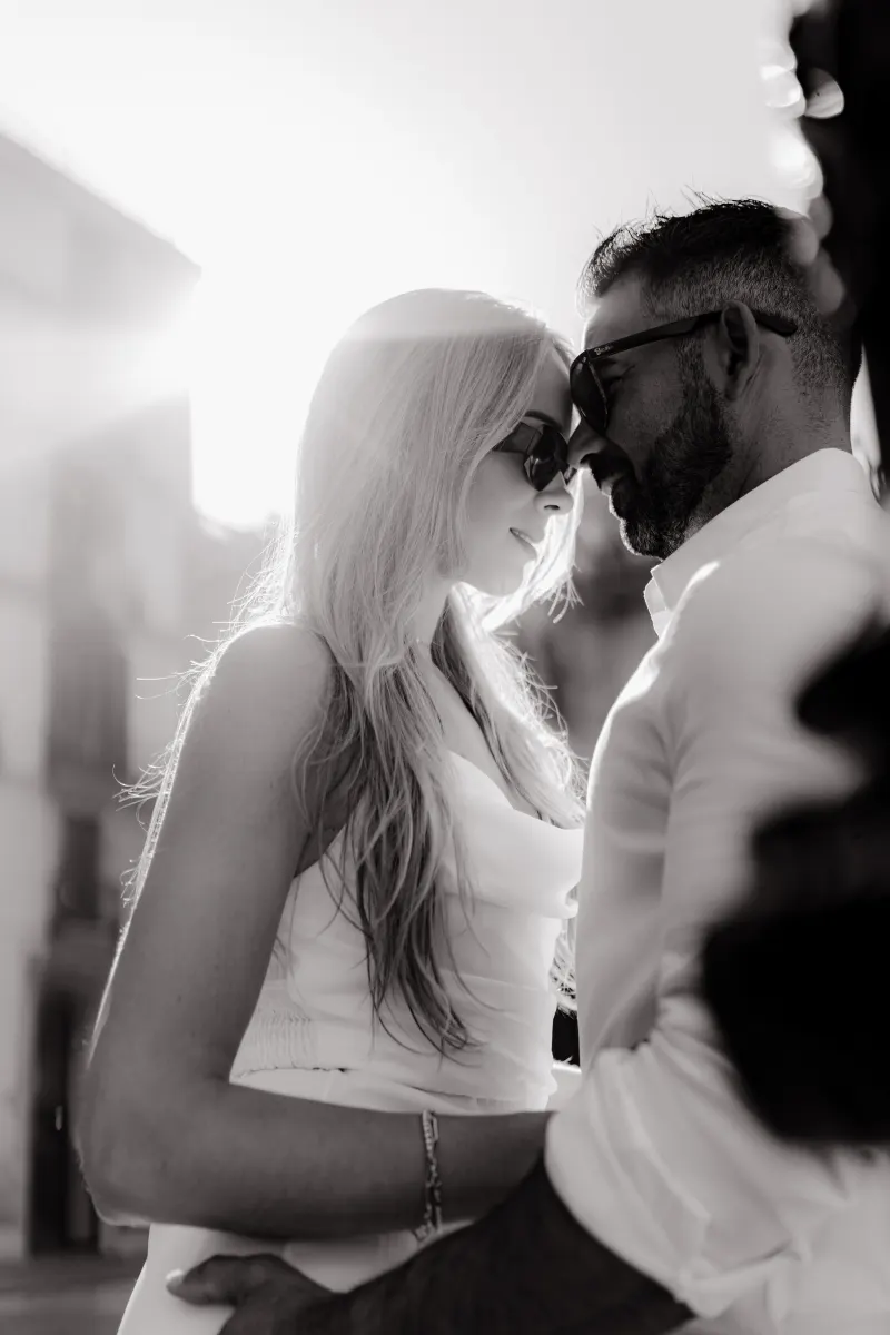 Couple in white outfits share a tender forehead touch in golden sunlight during a couples & engagements photoshoot.