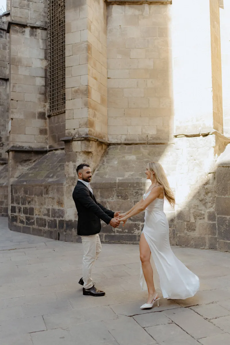 Couple laughing and dancing together in sunlight by historic stone walls during a couples & engagements photoshoot.