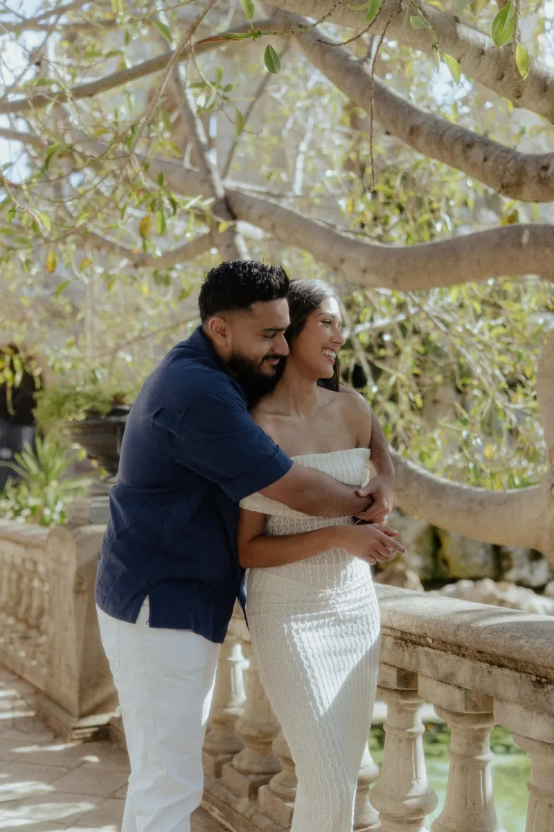 Couple laughing and embracing on a sunlit stone terrace, captured during a joyful couples & engagements photoshoot outdoors.