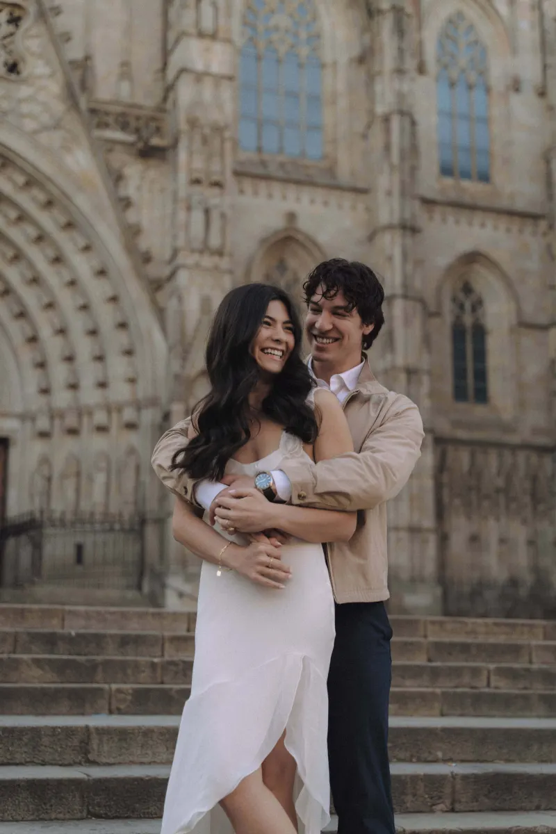 Couple laughing and embracing on cathedral steps during a couples & engagements photoshoot, sharing a candid moment.