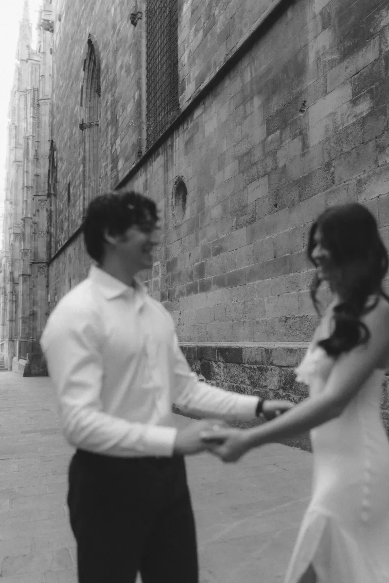 Couple laughing and holding hands on a quiet stone street during a couples & engagements photoshoot by a historic building.