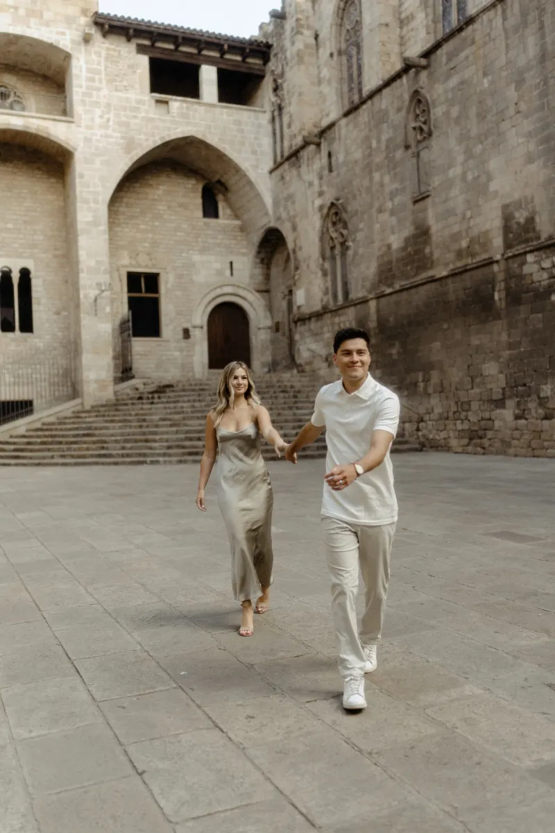 Couple laughing and holding hands while exploring a historic Barcelona courtyard during a Vacation Portraits photoshoot.