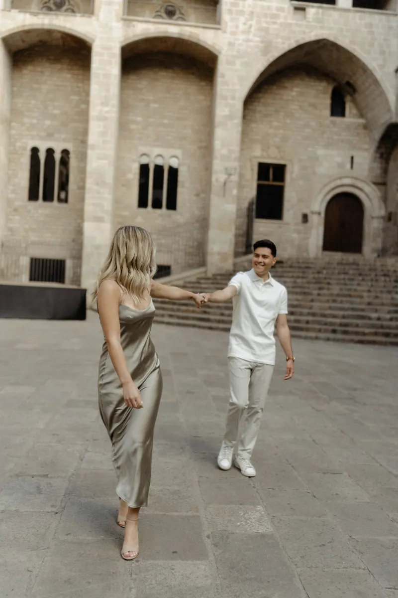 Couple laughing and holding hands while exploring a historic Barcelona square during a Vacation Portraits photoshoot.