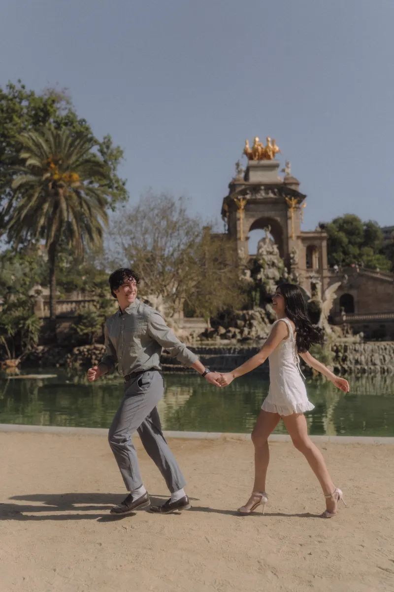 Couple laughing and holding hands while playfully walking by the fountain at Parc de la Ciutadella during an engagement shoot