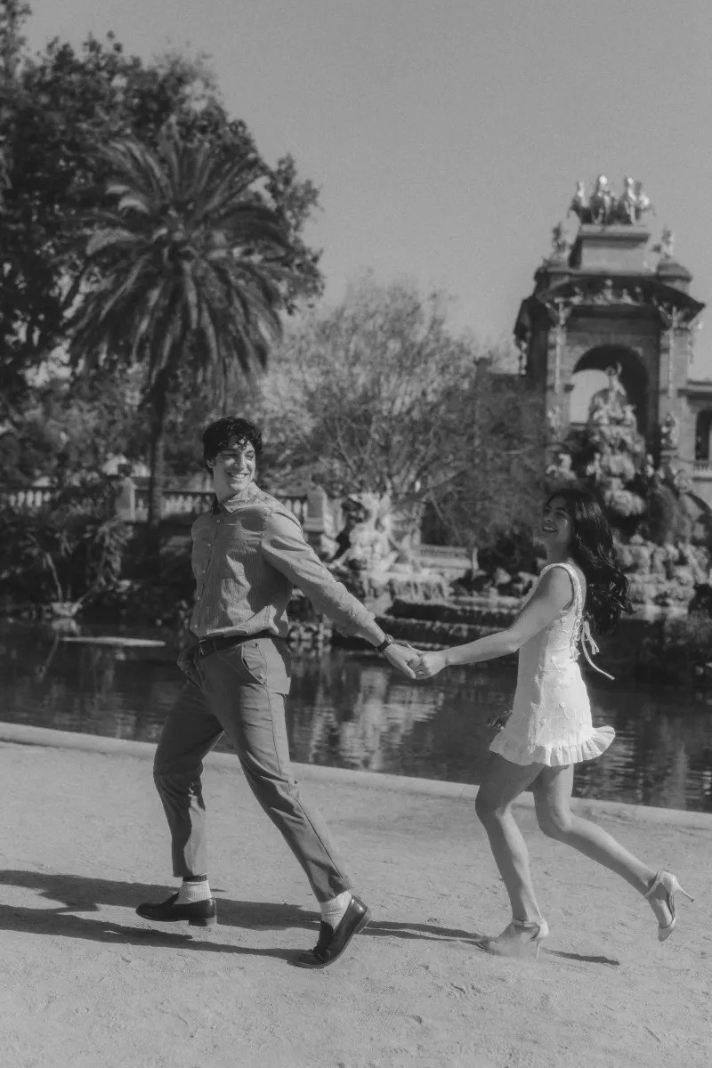 Couple laughing and holding hands while playfully walking by the fountain during a couples & engagements photoshoot.