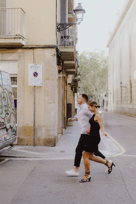 Couple laughing as they cross a quiet city street together, captured during a couples & engagements photoshoot session.