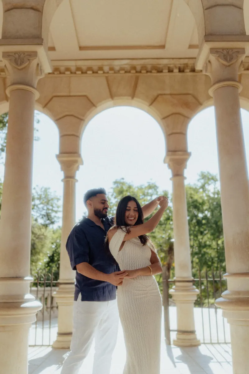Couple laughing as they dance together under elegant stone arches during a joyful engagement photoshoot.