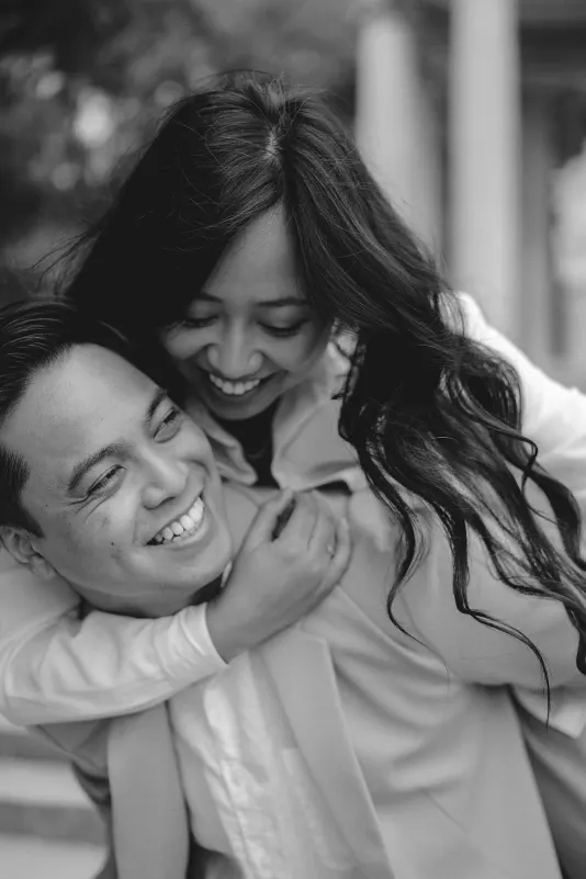 Couple laughing together as she gives him a piggyback ride, captured during a joyful couples & engagements photoshoot.