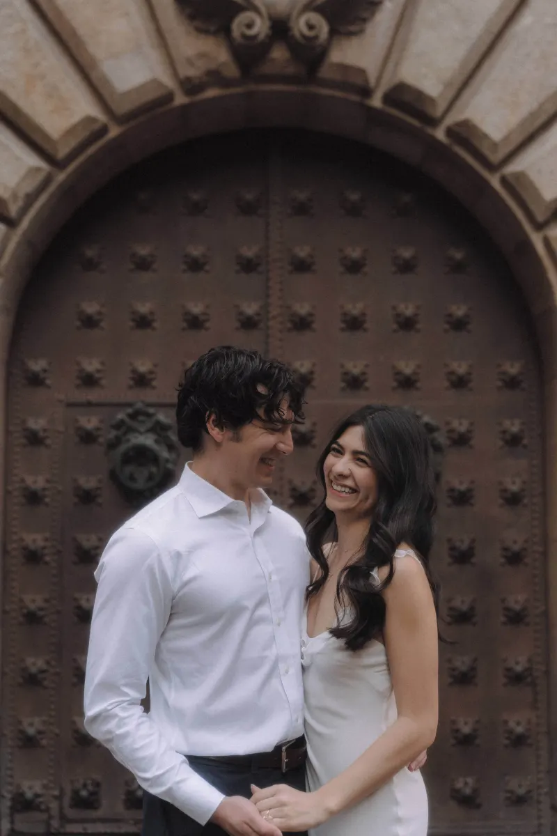 Couple laughing together in front of an ornate arched door during a couples & engagements photoshoot.