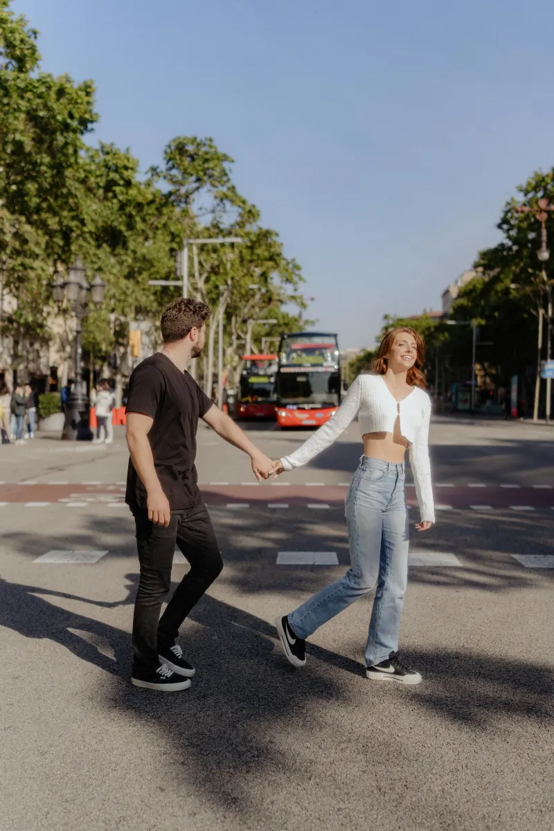 Couple laughs and holds hands while crossing a sunny city street during a couples & engagements photoshoot.