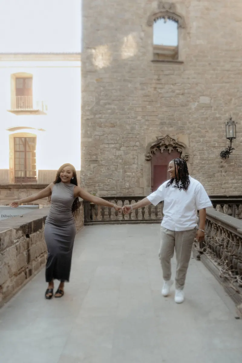 Couple laughs and holds hands while strolling through Barcelona’s Gothic Quarter during a surprise proposal photoshoot.