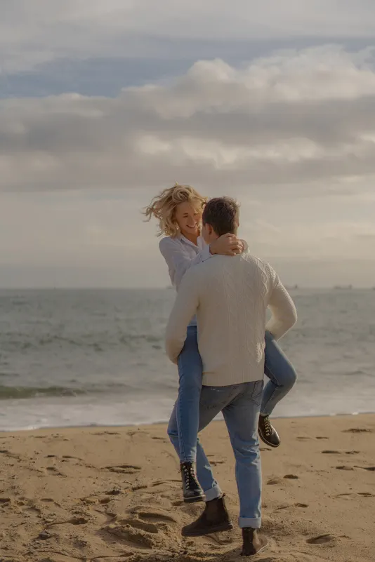 Couple laughs as he lifts her on the sandy Barcelona beach during a couples & engagements photoshoot.