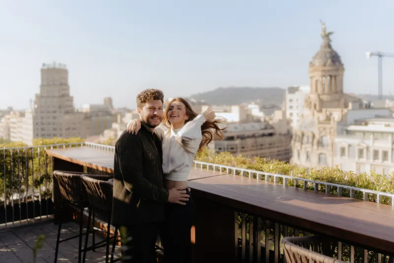 Couple laughs together on a sunlit rooftop, captured during a couples & engagements photoshoot with city views.