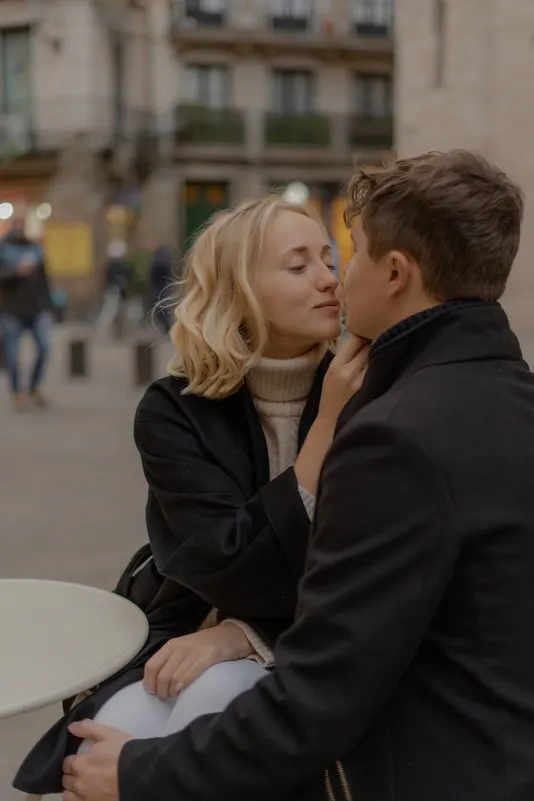 Couple leans in for a tender kiss at an outdoor café in Barcelona during a couples & engagements photoshoot.