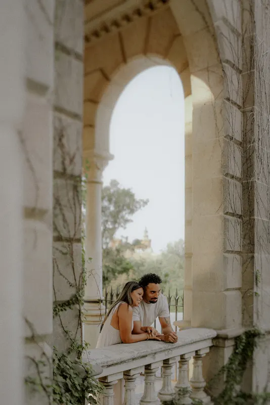 Couple leans together on a stone balcony, sharing a quiet moment during their engagement photoshoot in Parc de la Ciutadella.