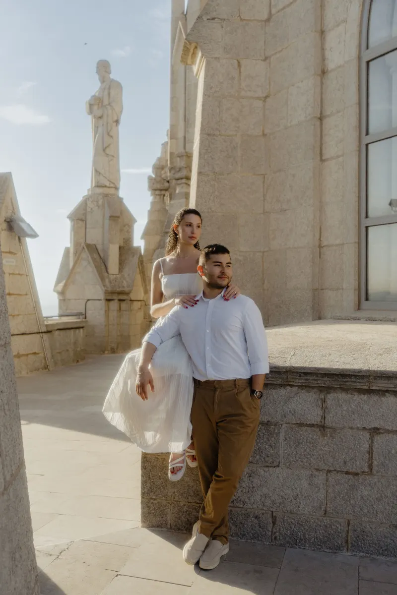 Couple poses on sunlit stone terrace, sharing a quiet, romantic moment during their engagement photoshoot.