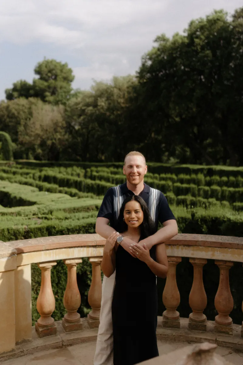 Couple poses together on a garden terrace, celebrating their engagement during a surprise proposal photoshoot.
