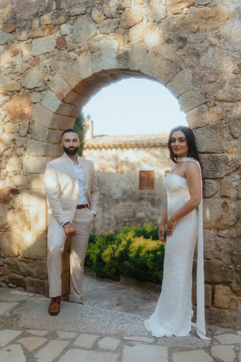 Couple poses under a rustic stone archway, celebrating their engagement during a surprise proposal photoshoot.