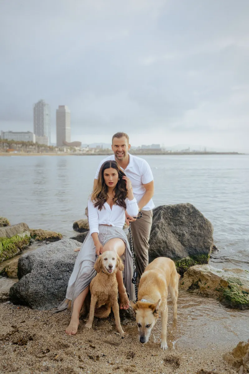 Couple posing with their two dogs on a city beach, capturing a candid moment during a couples & engagements photoshoot.