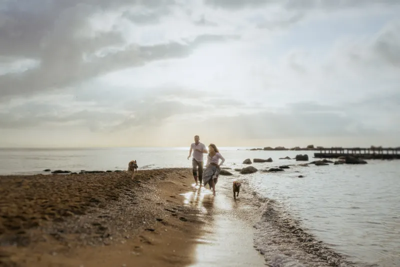 Couple running barefoot along the beach with their dogs at sunrise, captured during a couples & engagements photoshoot.