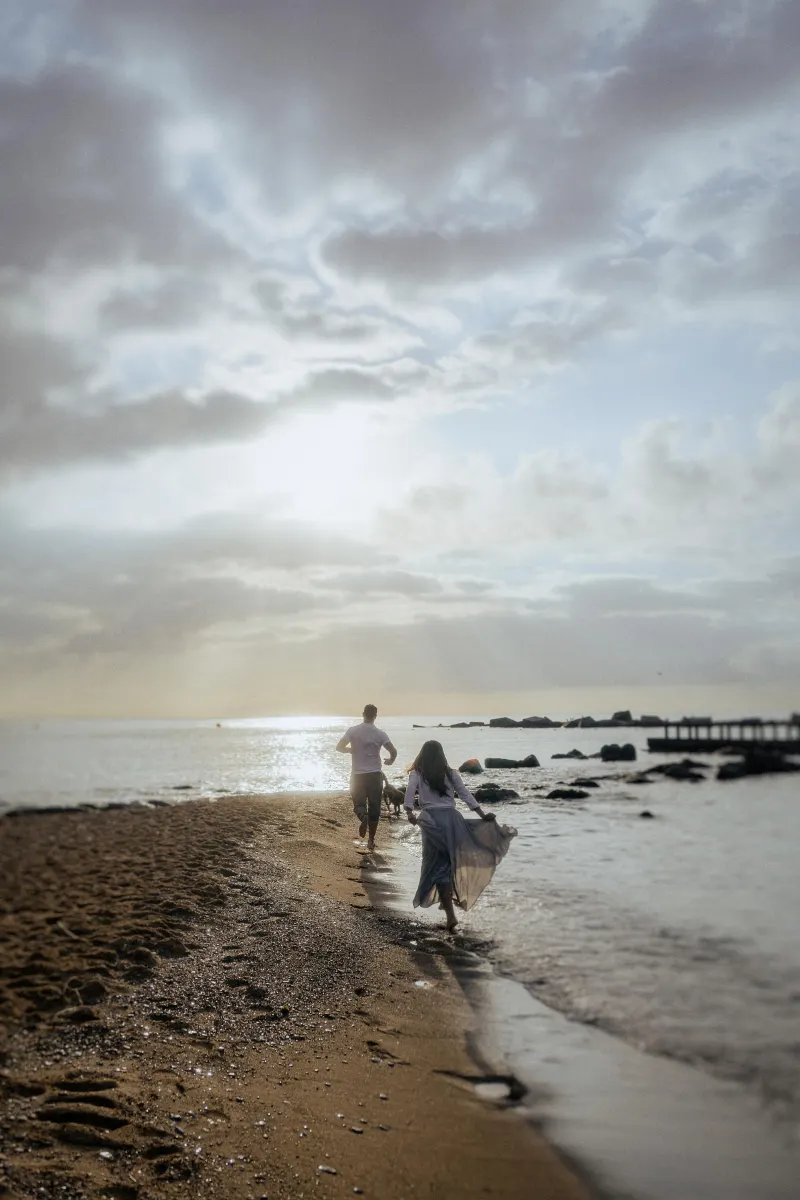 Couple running barefoot along the shoreline at sunrise, sharing a carefree moment during a couples & engagements photoshoot.