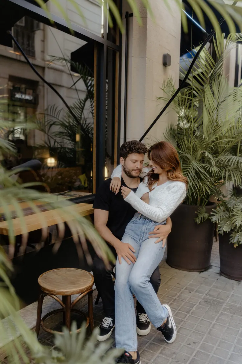 Couple shares a cozy, affectionate moment outside a city café during a couples & engagements photoshoot.