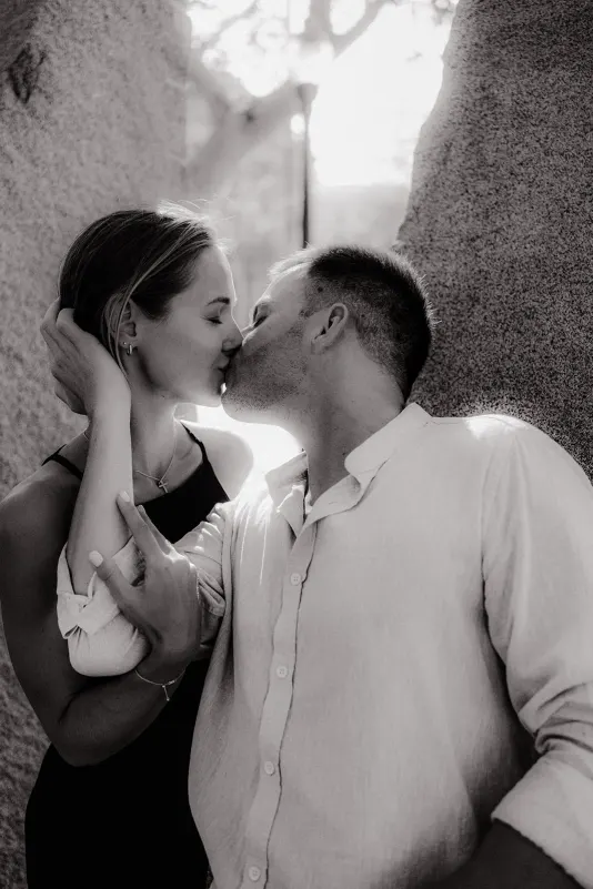 Couple shares a gentle kiss in soft sunlight between stone walls, captured during a couples & engagements photoshoot.