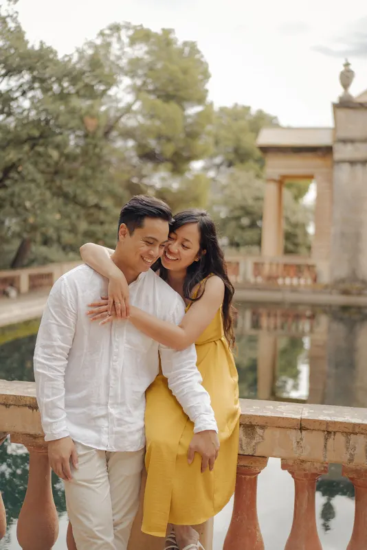 Couple shares a joyful embrace by a reflecting pool, captured during a couples & engagements photoshoot in the park.