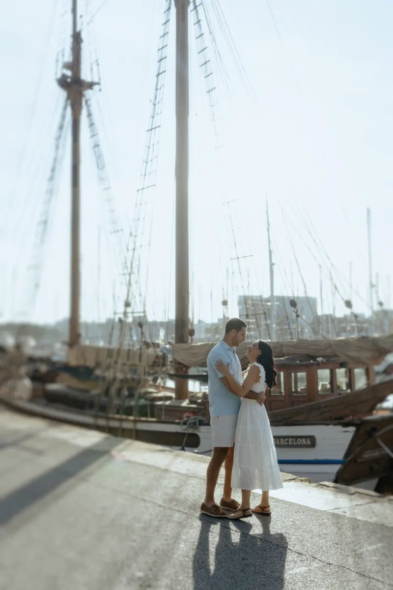 Couple shares a joyful embrace by sailboats at the marina, captured during a couples & engagements photoshoot.