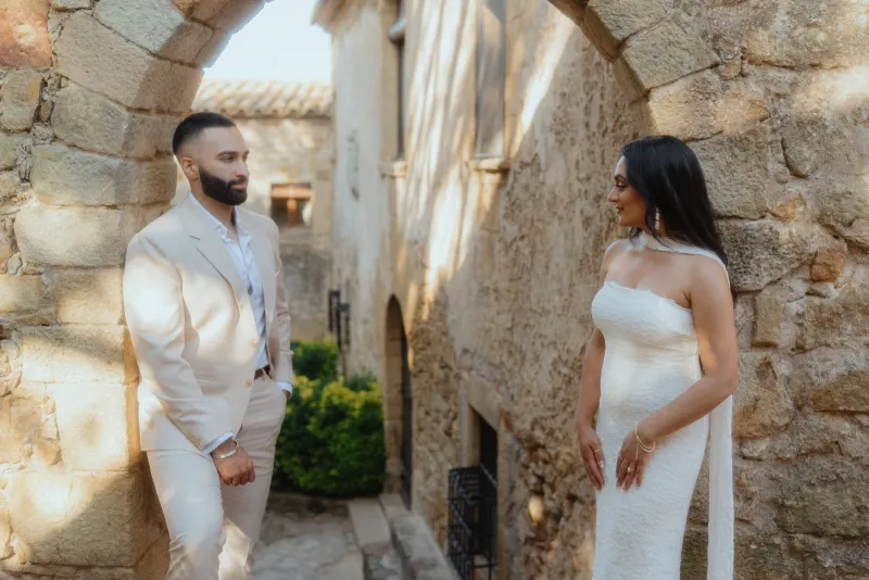 Couple shares a joyful glance beneath a stone archway after their surprise proposal photoshoot in a historic village.