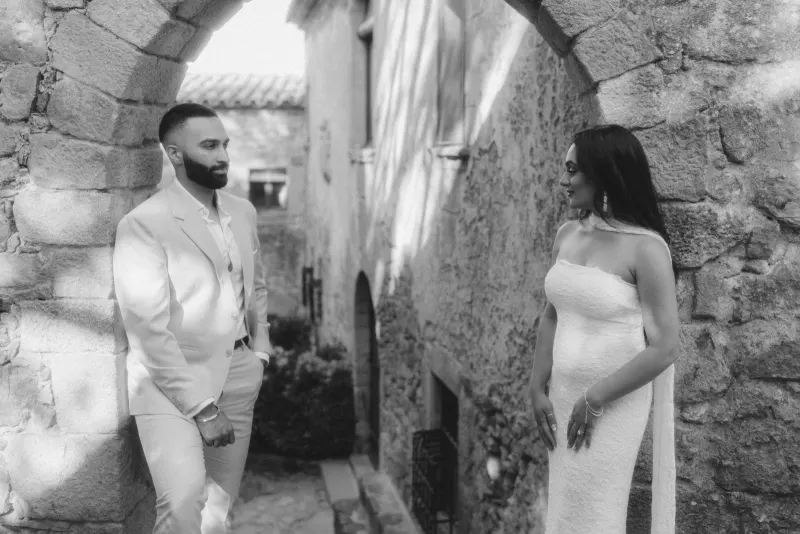 Couple shares a joyful glance beneath a stone archway during their surprise proposal photoshoot in a historic alley.