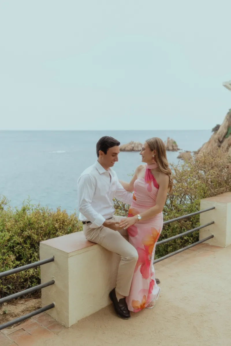 Couple shares a joyful, intimate moment by the ocean after a surprise proposal photoshoot on a scenic terrace.