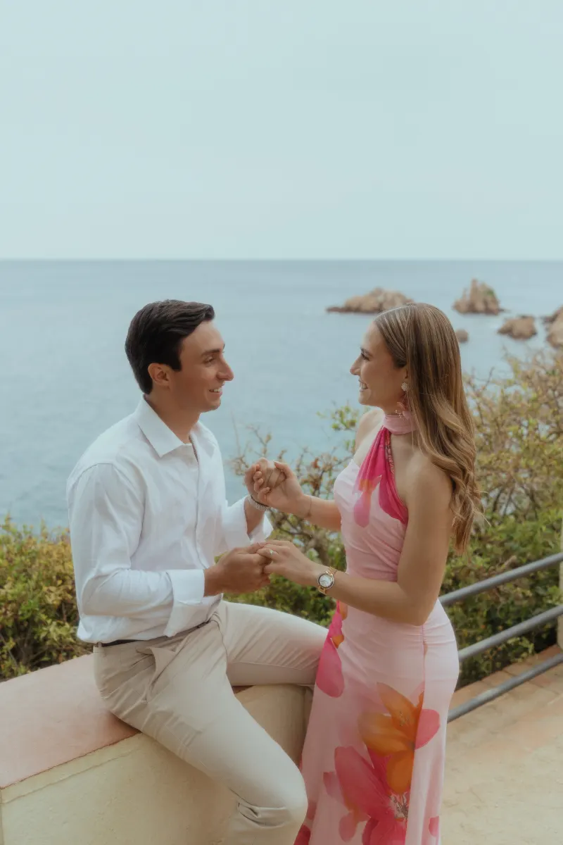 Couple shares a joyful, intimate moment holding hands by the ocean during a surprise proposal photoshoot.