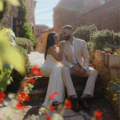 Couple shares a joyful moment after a surprise proposal, sitting on sunlit stone steps in a charming rustic village.