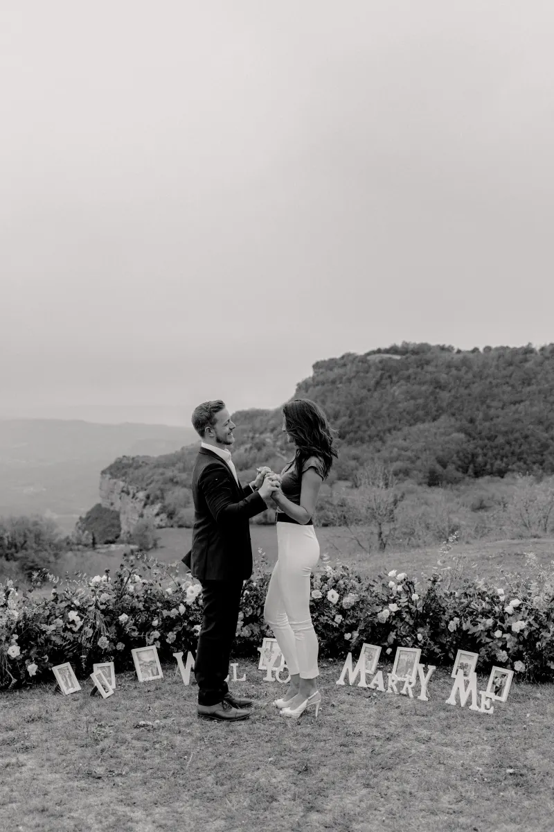 Couple shares a joyful moment on a flower-lined hillside after a surprise proposal, captured during a professional photoshoot