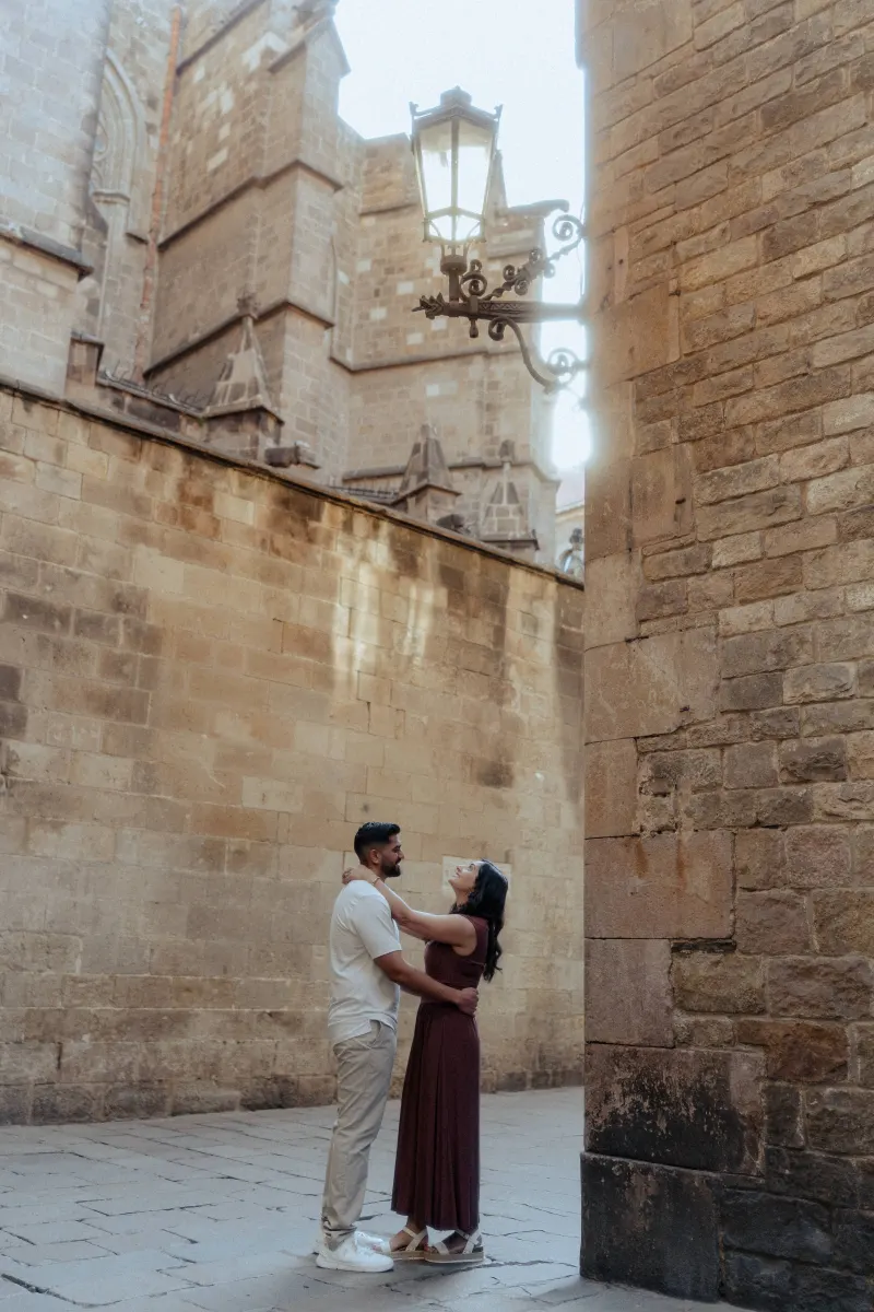 Couple shares a loving embrace and smile during an engagement photoshoot in a sunlit historic European alleyway.