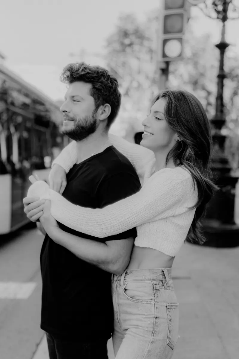 Couple shares a loving embrace on a city street, captured during a couples & engagements photoshoot in natural light.