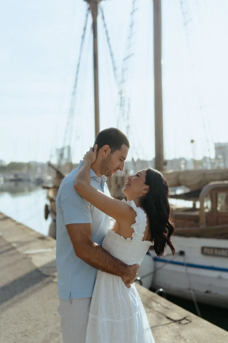Couple shares a loving embrace on a sunlit marina pier, captured during a couples & engagements photoshoot session.