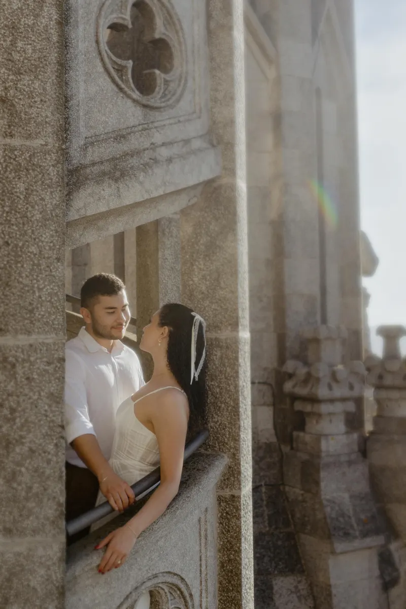 Couple shares a loving gaze on a sunlit stone balcony, captured during a romantic couples & engagements photoshoot.