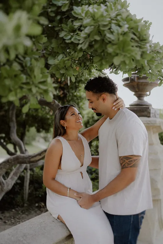 Couple shares a loving gaze under leafy branches during a romantic engagement session in a historic garden.