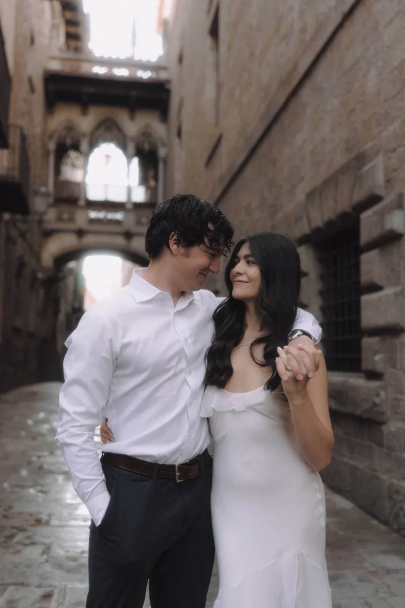 Couple shares a loving gaze while holding hands in Barcelona’s Gothic Quarter during a couples & engagements photoshoot.