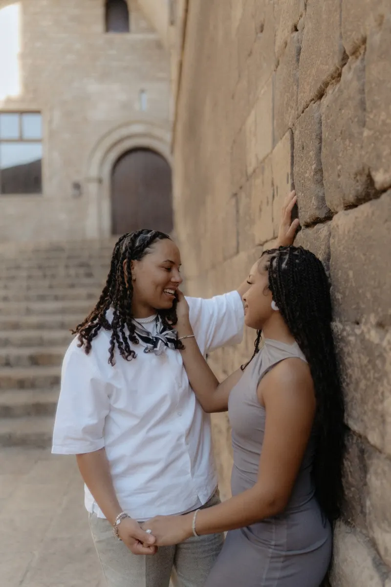 Couple shares a loving, intimate moment by a stone wall during their surprise proposal photoshoot in Barcelona.
