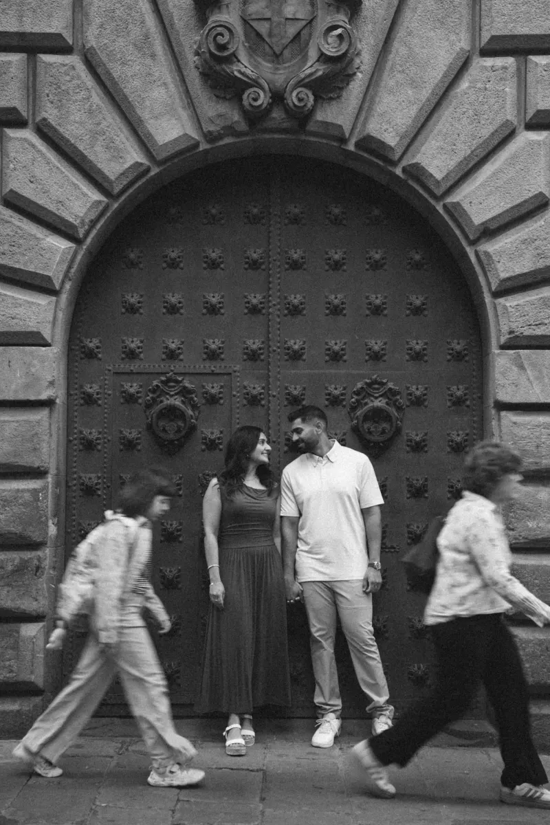 Couple shares a loving look while holding hands in front of a grand historic doorway during their engagement photoshoot.