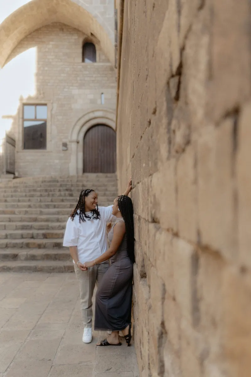 Couple shares a loving, playful moment by ancient stone steps during their surprise proposal photoshoot in Barcelona.