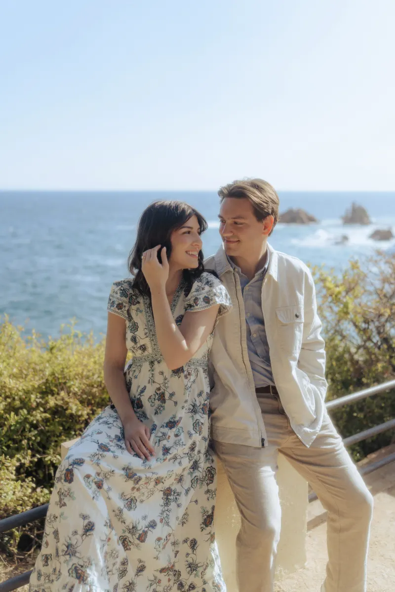 Couple shares a loving smile by the ocean, captured during a surprise proposal photoshoot on a bright afternoon.