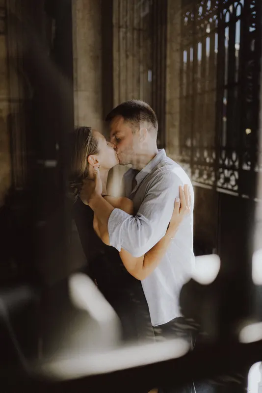 Couple shares a passionate kiss in a sunlit hall, captured during a couples & engagements photoshoot.