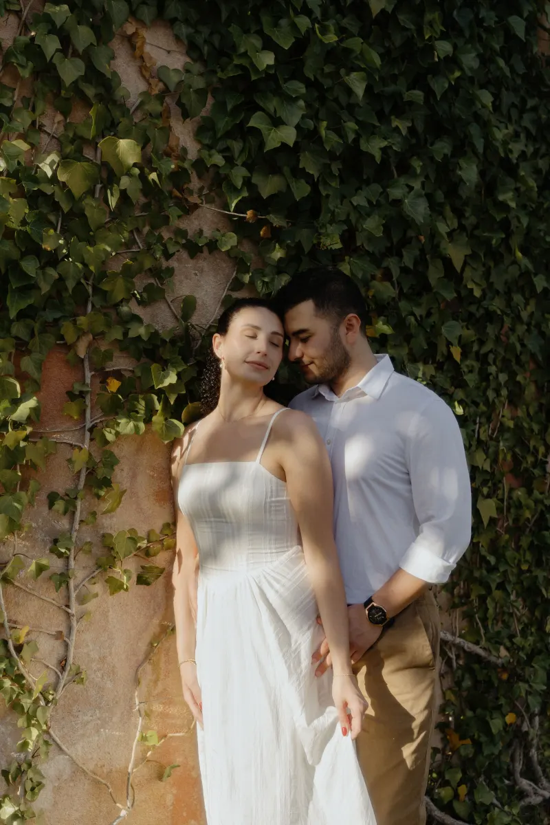 Couple shares a peaceful embrace against a sunlit ivy wall during a romantic couples & engagements photoshoot.