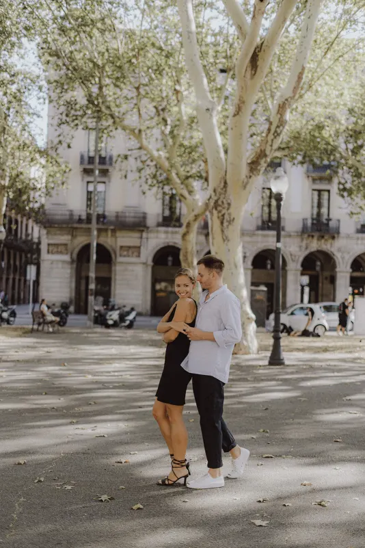 Couple shares a playful embrace beneath city trees, radiating joy during a couples & engagements photoshoot outdoors.